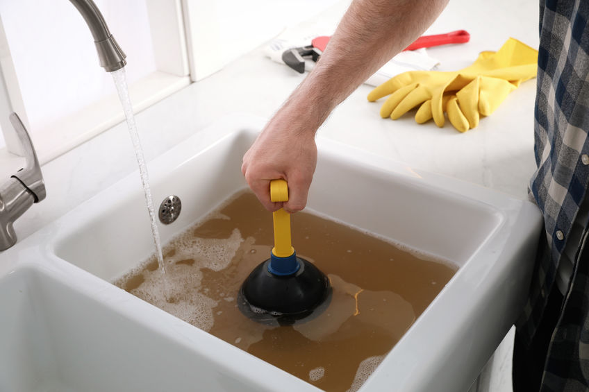 Man Using Plunger to Unclog Sink Drain in the Kitchen | Miller Plumbing & Drainage Ltd.