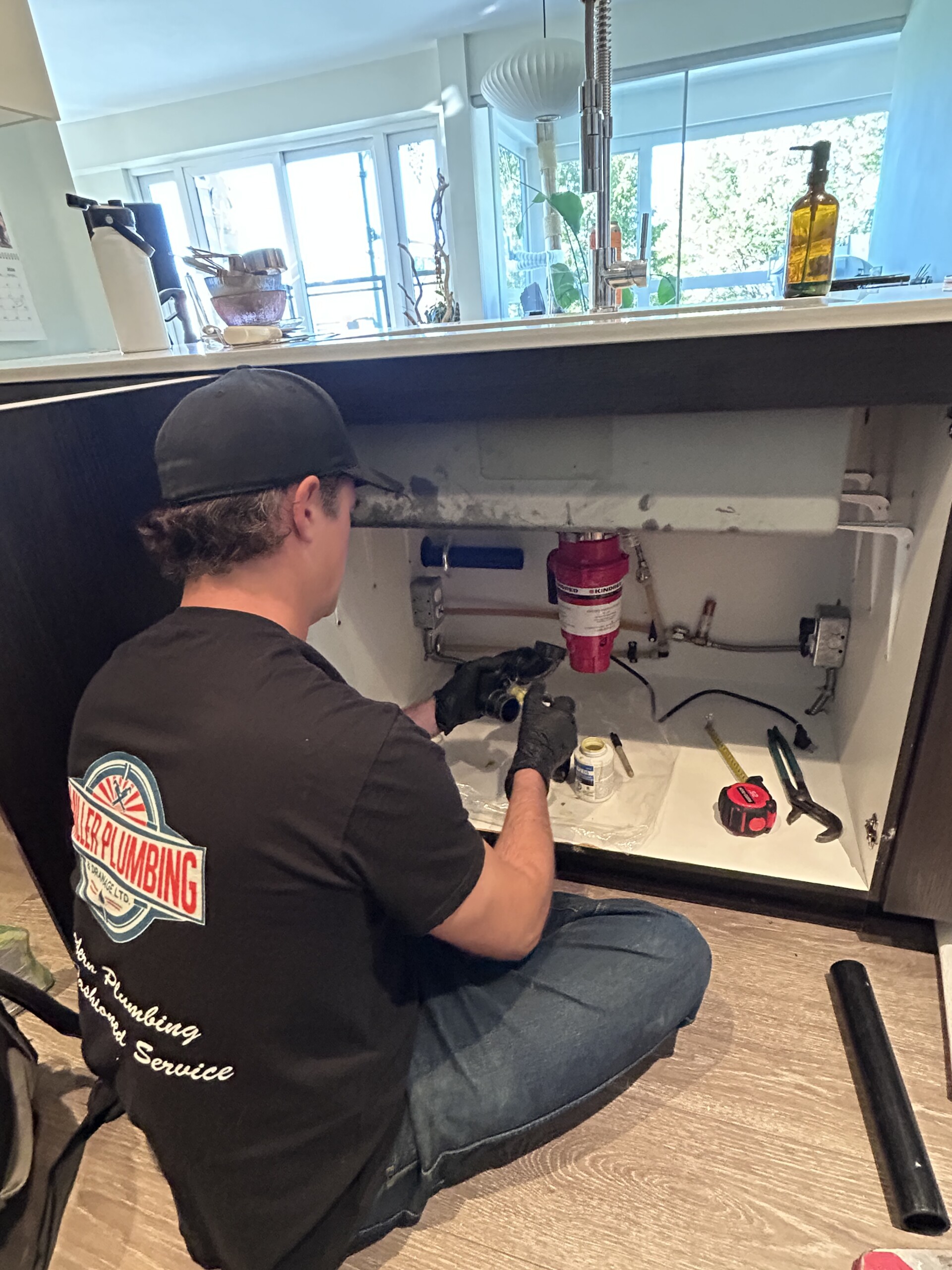 Garburator installation – Vancouver kitchen Miller Plumbing connecting a new garburator drain under a kitchen sink